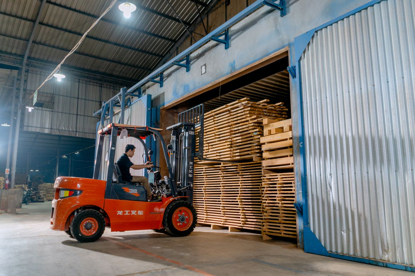 Forklift operator handling stacked wood inside an industrial warehouse