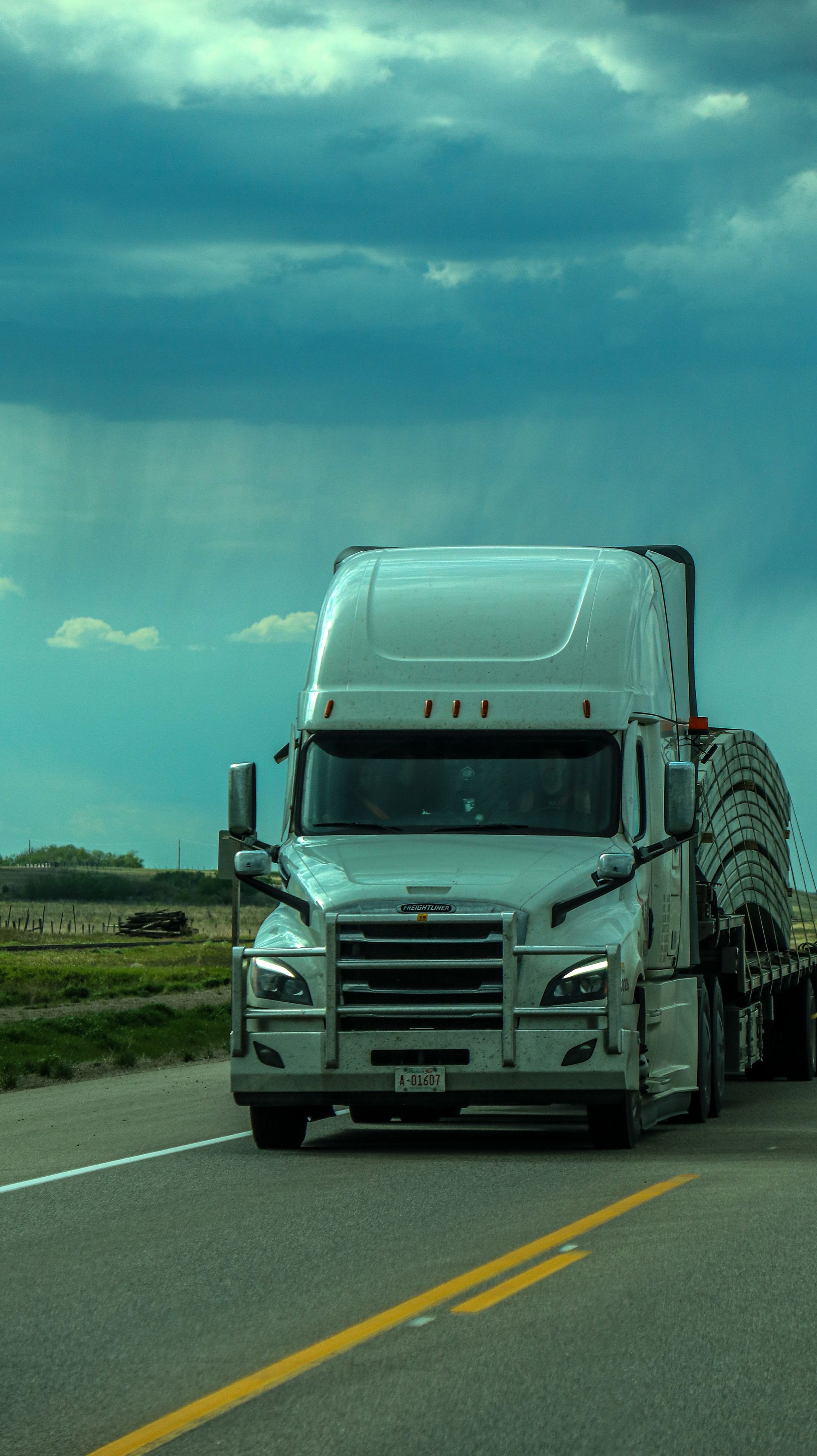 White American-style semi-truck transporting a covered load on a flat highway
