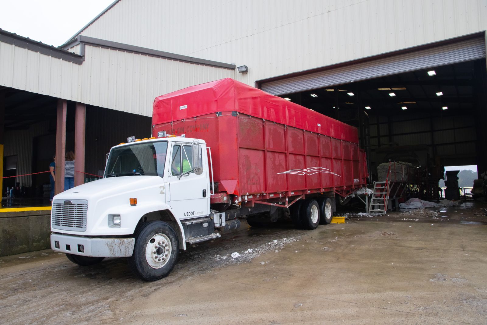 American truck with a red cargo trailer beside a warehouse loading area