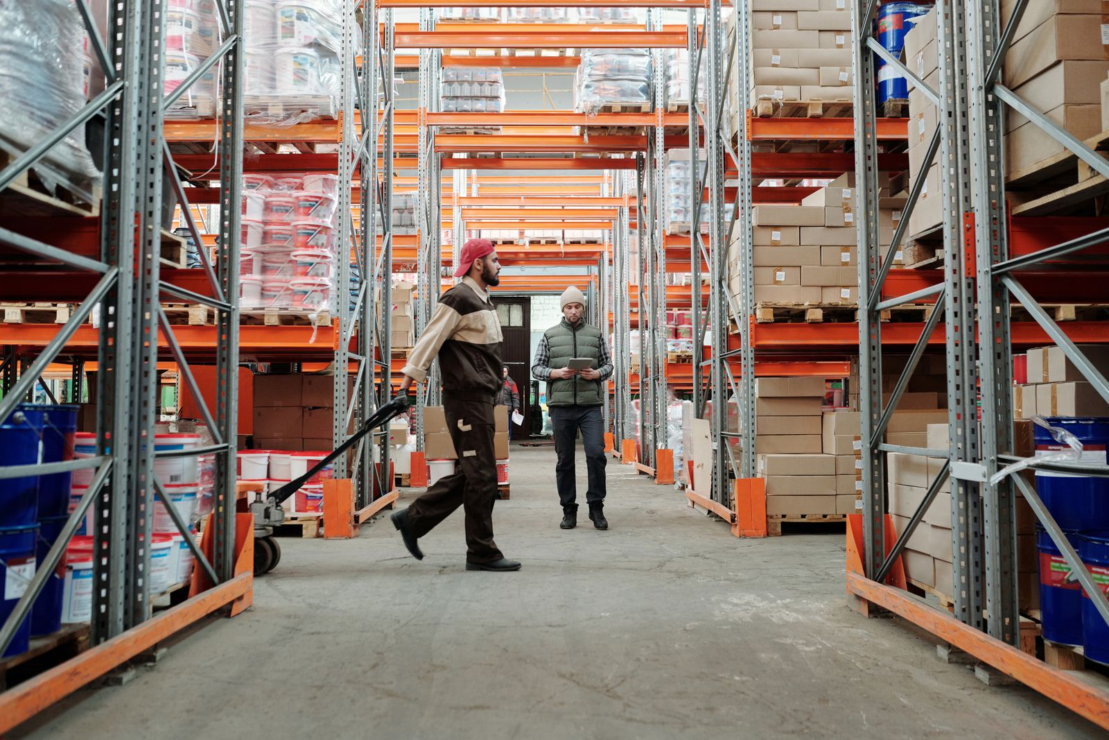 Warehouse employees checking information and moving a pallet jack